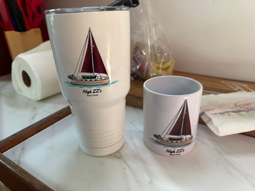 Customer's white custom 30 oz tumbler with sailboat artwork, shown next to a smaller matching mug on a counter.