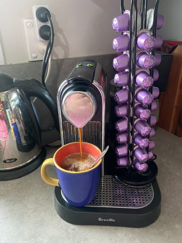 Customer brewing a dark coffee with a Blend 12 capsule, with a stand full of the purple capsules on the side.