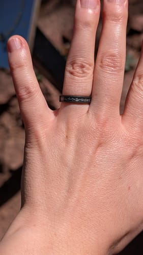 A customer's hand wearing the Black Meteorite ring with a speckled inlay outdoors in the sun.