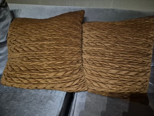 Anmelderens to myke, karamellfargede putetrekk i flettet velur på en grå sofa.