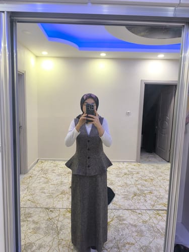 Yorumcu, peplumlu kahverengi tüvit yelek etek takımını ayna karşısında gösteriyor.