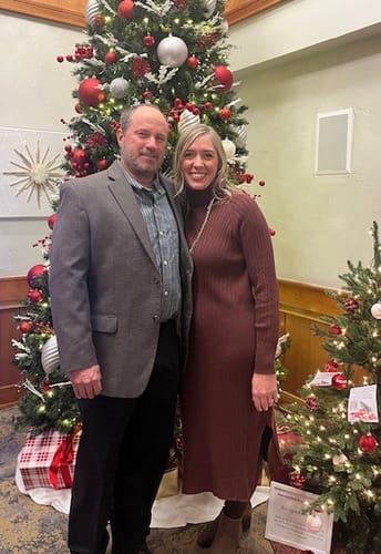 Customer wearing the Ribbed Sweater Midi Dress in a dark red color, standing with a man by a Christmas tree.