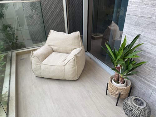Customer's comfortable Olefin Lounge Chair placed on a light-wood balcony next to a potted plant.