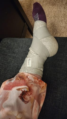 A customer's foot resting, wearing the gray Premium Bamboo Ankle Support wrapped over their sock.