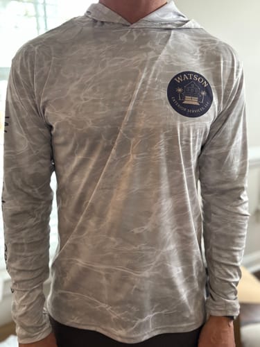 Customer wearing the front of a light grey Mossy Oak UPF Hooded Shirt with a custom business logo on the chest.