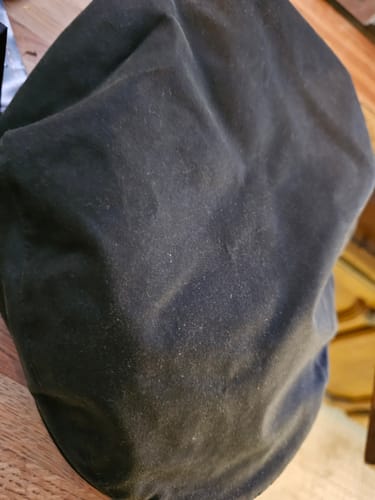 A customer's dark Waxed Cotton Flat Cap, showing the texture of the fabric in a close-up view.