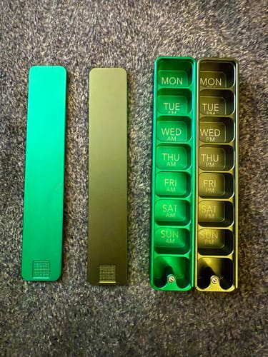 Customer's Weekly AM-PM Pill Case 2.0 laid out on a carpet, separated into its green and dark halves.