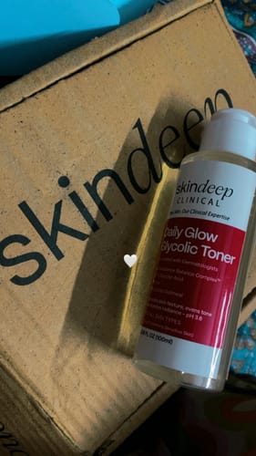 Customer's bottle of Daily Glow Glycolic Toner with a red label, shown in front of its branded cardboard box.
