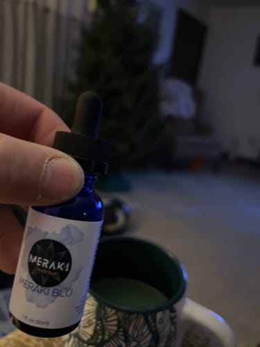 Customer's hand holding a blue bottle of Meraki Blu Methylene Blue next to a mug.