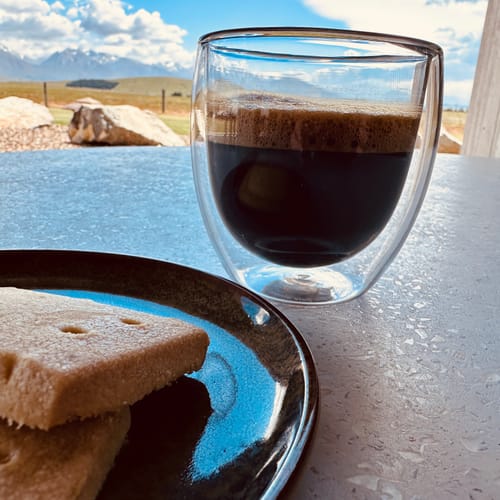 Customer's Colombian coffee with a rich crema, served in a double-walled glass with a mountain view.