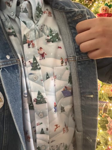 A reviewer opens their denim jacket, revealing the festive Rudolph the Red-Nosed Reindeer 'Stop Motion Wonderland' shirt.