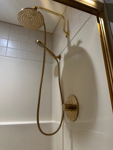 Reviewer's gold 1-Spray Dual Shower Head Set installed with a custom S-shaped arm in a white shower.