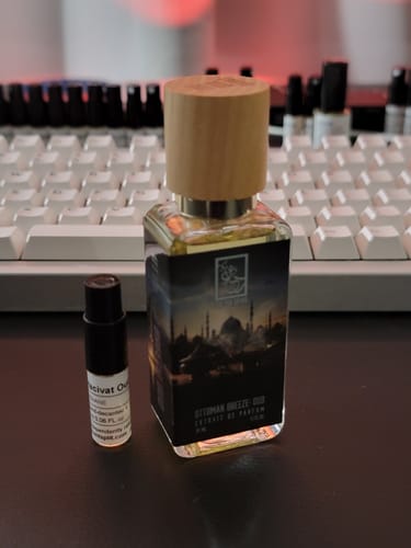 Reviewer's bottle of Ottoman Breeze: Oud with a wooden cap, sitting next to a smaller sample vial on a desk.