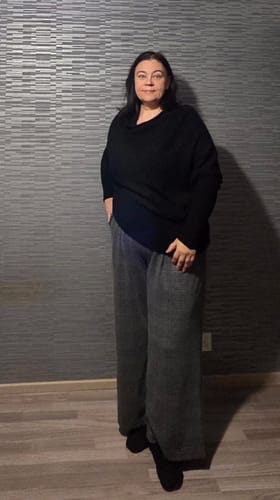Customer wearing the black Asymmetric Draped sweater with grey trousers, showing its relaxed drape.