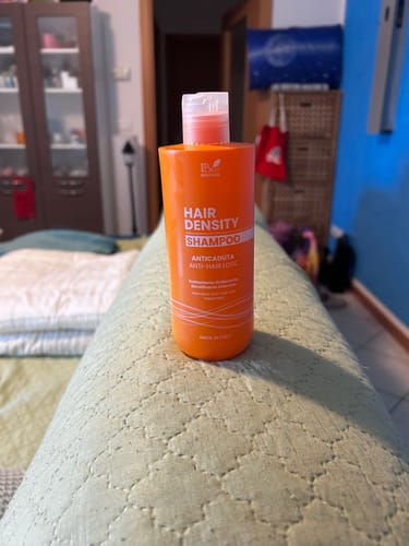 Il cliente mostra il flacone arancione dello shampoo Hair Density - Anti Caduta, appoggiato sul bracciolo di un divano.