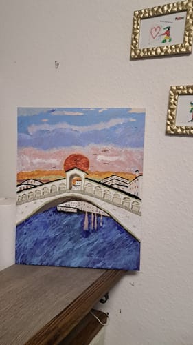 Kunde zeigt sein fertiges Malen-nach-Zahlen-Gemälde, das eine Brücke über Wasser bei Sonnenuntergang darstellt.