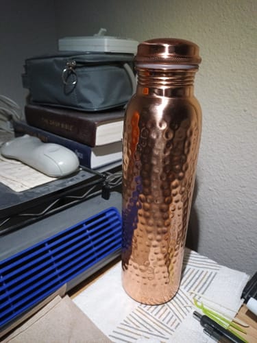 Customer's shiny, hammered Himalayan Ayurvedic Pure Copper Bottle standing on a desk.