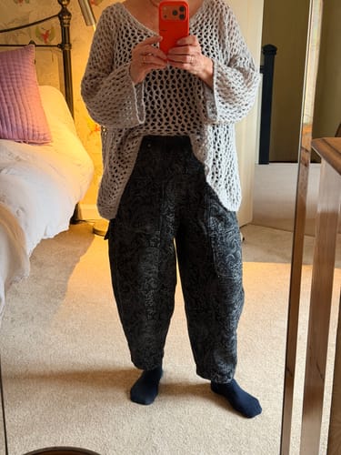 A reviewer stands in front of a mirror wearing the dark, patterned winter retro flower harem pants.