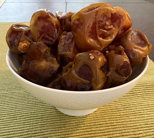 Customer's glossy Organic Barhi Dates piled high in a white bowl on a green placemat.