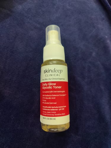 Customer's bottle of Daily Glow Glycolic Toner shown on a dark blue surface.