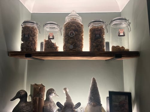 Customer's pork scratchings from their bundle displayed in five decorative glass jars on an illuminated wooden shelf.