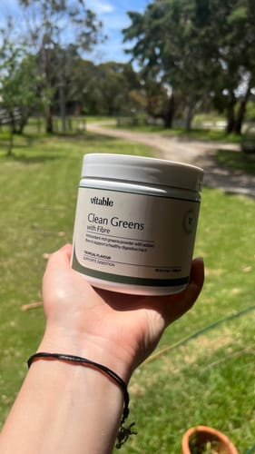 Customer holding the tub of Clean Greens Powder + Fibre in a sunny, outdoor setting.