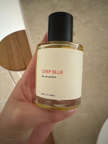 Customer holding a clear bottle of Deep Blue perfume, showing the white label.