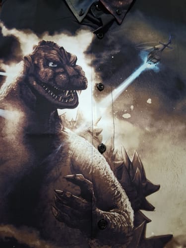 Close-up of a reviewer's Godzilla "The King Arrives" shirt, showing the detailed artwork of Godzilla being attacked by a helicopter.