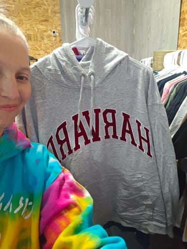 A reviewer stands next to a grey hooded Harvard University sweatshirt from the wholesale mix, hanging on a rack.