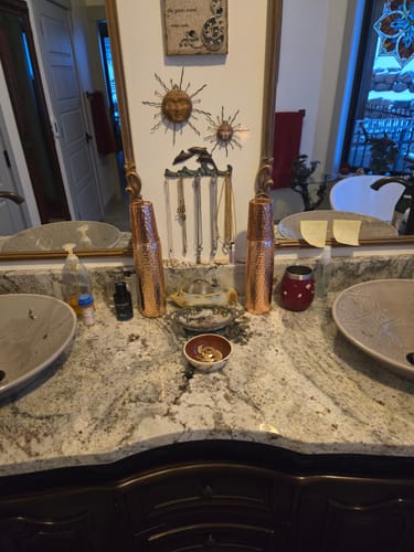 Reviewer's two hand-hammered copper water bottles on a granite bathroom countertop.