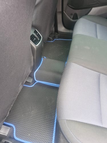 Klient pokazuje czarne dywaniki samochodowe o strukturze plastra miodu z niebieskim obszyciem, zamontowane na tylnych siedzeniach.