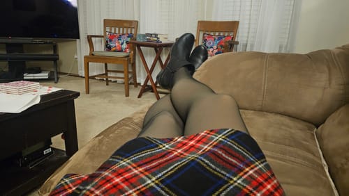 Customer relaxing on a couch wearing sheer Toast fleece-lined tights with a plaid skirt.