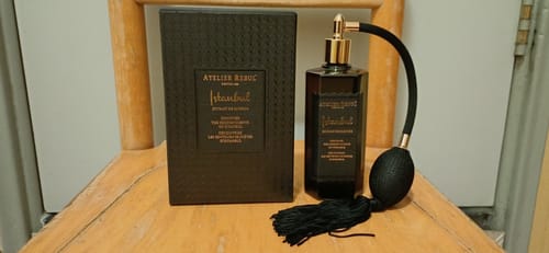 Recensent toont de fles Istanbul Extrait de Parfum met verstuiver naast de donkere doos op een houten stoel.