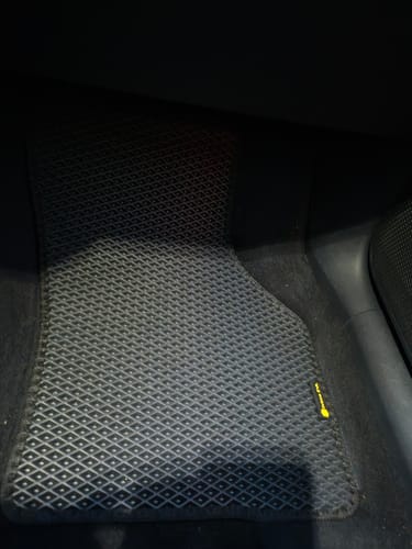 Recenzent pokazuje czarny, dopasowany dywanik samochodowy umieszczony na podłodze z przodu pojazdu.