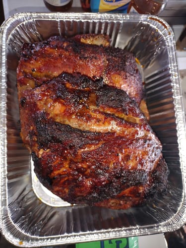 Customer's finished pork roast with a dark, seasoned crust, resting in a foil pan.