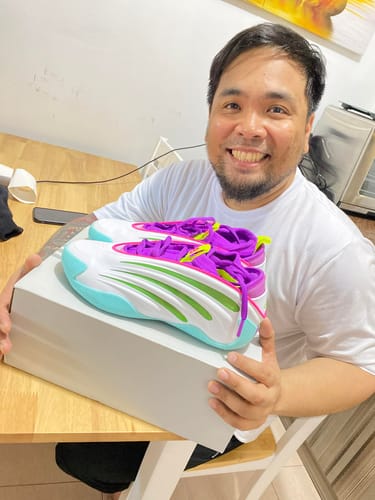 A smiling reviewer holds up their new, colorful adidas Harden Volume 9 Basketball Shoes over the shoebox.