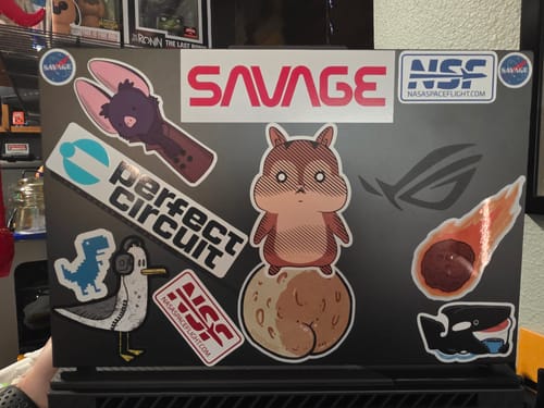 Customer's NSF-Logo stickers applied to the back of a dark gray laptop among other various decals.