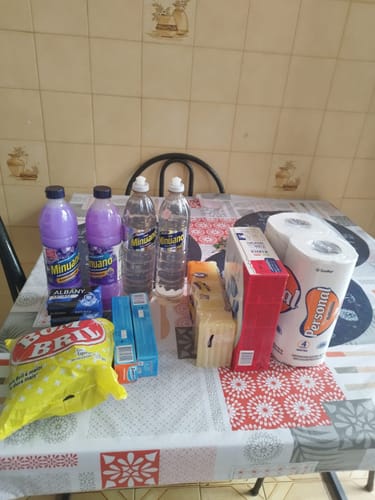 Cliente exibe sobre uma mesa os vários produtos que recebeu em sua Cesta Kit Limpeza Plus.