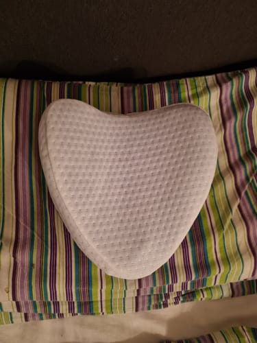 Kundes hvide, kileformede knæpude ligger på et stribet pudebetræk.