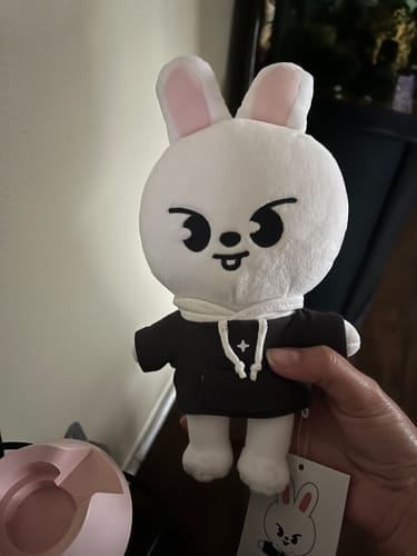 A customer's hand holding the white Leebit SKZOO plush toy, which is wearing a small black hoodie.