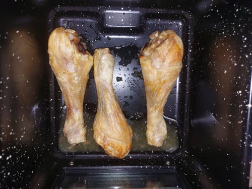 Clientul arată trei pulpe de pui rumenite, gătite în cuva cu acoperire din piatră Maifan a friteuzei Novio StonePro.