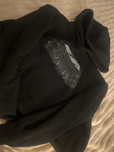 A customer's black DCG84 Hoodie with a large graphic on the chest, lying on a textured surface.