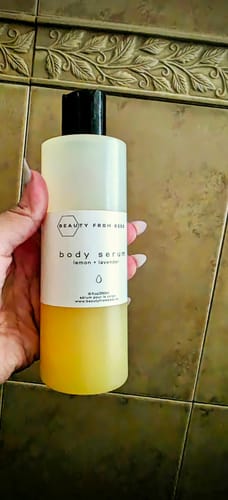 Reviewer holding a bottle of Lemon + Lavender Body Serum, showing the two-toned clear and yellow liquid.