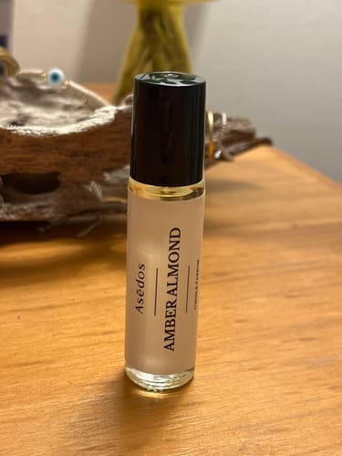 Customer's Amber Almond Perfume Oil in a frosted glass roll-on bottle, standing on a wooden table.