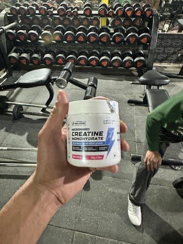 Customer holding a white tub of Wellcore Micronised Creatine Monohydrate in a gym setting.