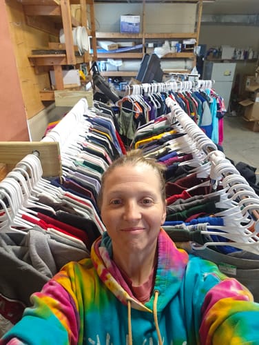 Reviewer taking a selfie with their large order of Wholesale Branded Sweatshirts hanging on racks.