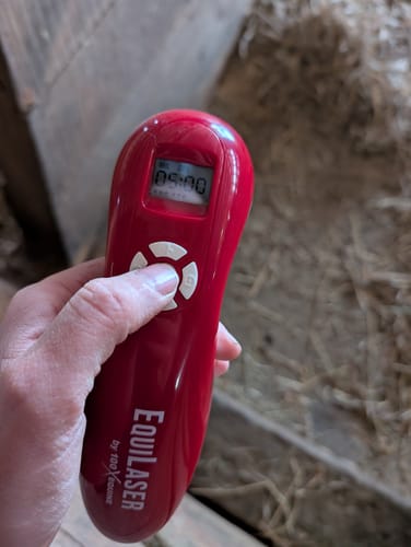 Customer's hand holding the red EquiLaser cold laser device, with their thumb resting on the control buttons.