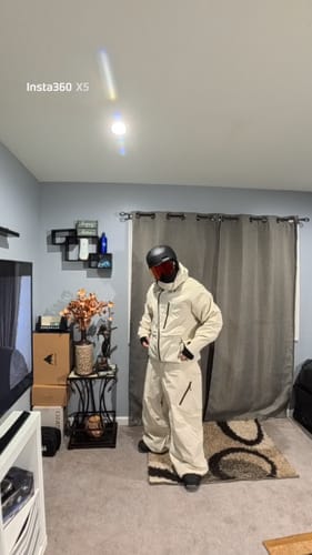 Reviewer standing indoors wearing the white waterproof snow jacket with matching pants and a helmet.