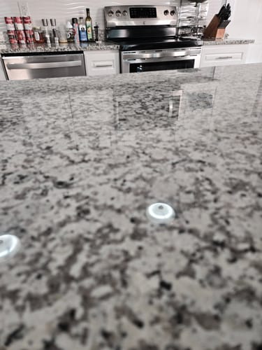 Customer's close-up of a shiny granite countertop reflecting the kitchen after using the Multi-Surface Concentrate.