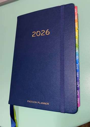 Customer's navy blue 2026 Weekly Hardcover Planner with colorful monthly tabs on the side.